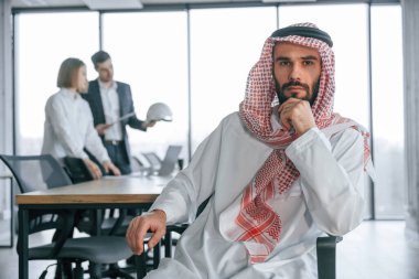 Kameraya bakıyorum. Geleneksel kıyafetli Müslüman işadamı ve görevde meslektaşları.