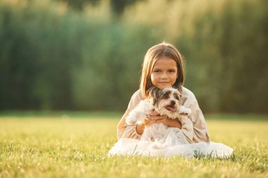 Ön manzara, yan yana oturmak. Tatlı küçük kız köpekle birlikte sahada..