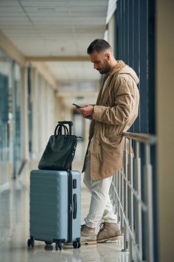 Akıllı telefon ellerde. Havaalanında genç yakışıklı bir adam var..