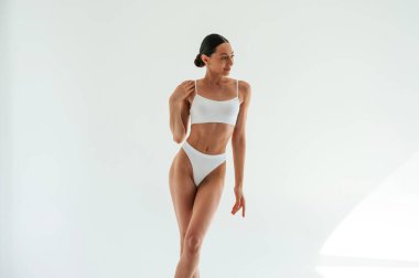 Durup poz vermek. Beyaz arka planda zayıf vücut tipi olan beyaz iç çamaşırlı bir kadın..