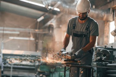 Açı öğütücü ellerinde. Gri üniformalı genç fabrika işçisi.