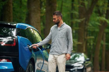 Genç adam şarj aletini elektrikli otomobil soketine takıyor..