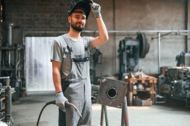 Mola verdim. Kaynak ekipmanlarıyla. Gri üniformalı genç fabrika işçisi.