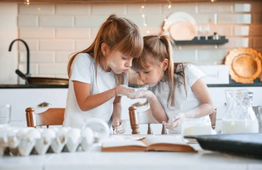 Un kullanarak. İki küçük kız mutfakta çelenklerle yemek hazırlıyor..