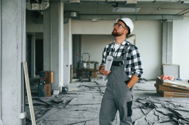 Projeyi planlıyorum, kağıtlarla. Bitmemiş odada üniformalı inşaat işçisi..