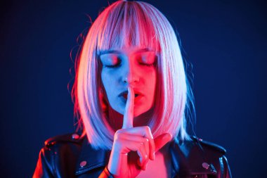 Parmaklar dudaktan, sessizlik. Beyaz saçlı kadın stüdyoda neon renkli..