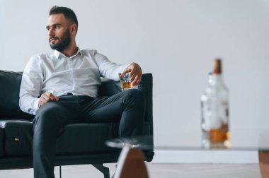 Kanepede oturuyor. Alkolik genç adam içeride..