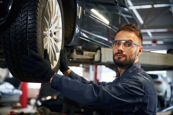 Смотрю в камеру. Авторемонтник в гараже с автомобилем.