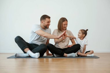 Çak bakalım. Anne, baba ve kızı evde yoga yapıyor..