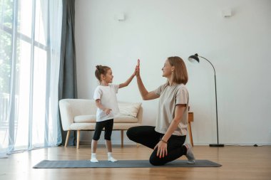Aferin, çak bir beşlik. Küçük kızı olan genç bir kadın evde yoga yapıyor..