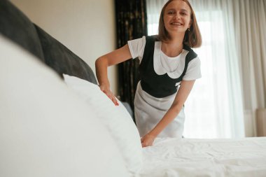 Yatak için yeni bez. Genç oda hizmetçisi otel odasında..