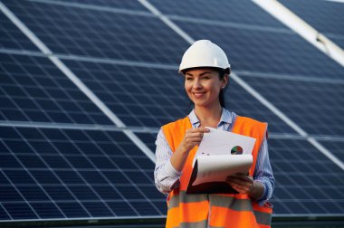Not defteri elimde. Üniformalı kadın işçi mühendisi güneş panellerinin yakınında..