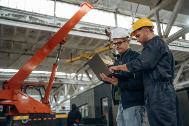 Laptoptan bilgi okunuyor. İki erkek fabrika işçisi depoda..