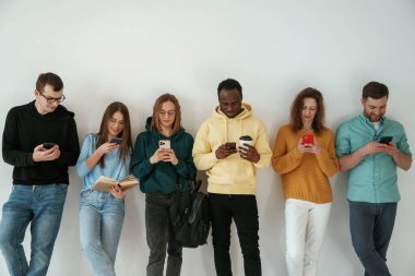 Elinde akıllı telefonlarla. Bir grup genç beyaz arka planda duruyor..