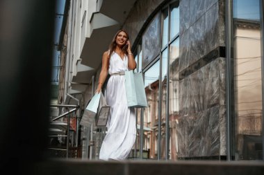 Telefonla konuşmalar. Şık bir kadın alışveriş çantasıyla dışarıda, binanın yanında..