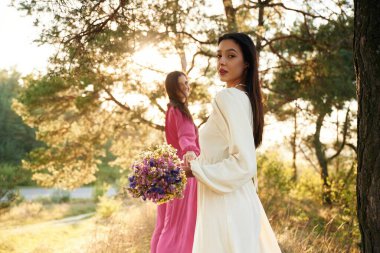 Kadın bir buket çiçekle gitmek istiyor. Güzel lezbiyen çift doğada birlikte..