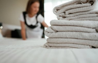 Yatağın üzerinde bir sürü yeni bez var. Genç oda hizmetçisi otel odasında..
