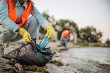 Kıyıda. Bir gönüllü çamurlu bir sahilde çöp topluyor..