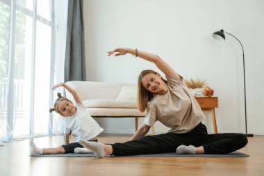 Kenarda, geriniyor. Küçük kızı olan genç bir kadın evde yoga yapıyor..