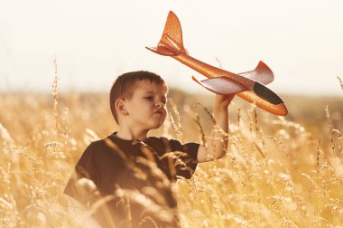 Kırmızı oyuncak uçağı tutuyor, oynuyor. Küçük çocuk yazın dışarıda eğleniyor..