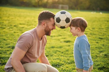 Futbol topu, kafasından tutmak, eğlence. Mutlu baba ve oğlu yazın sahada olurlar..