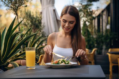 Tabaktaki yiyecekleri yemek. Güzel, genç bir bayan restoranın dışında, masanın yanında..