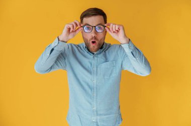 Şok olmuş, dokunaklı gözlükler. Mavi gömlekli çekici adam sarı arka plana karşıdır..