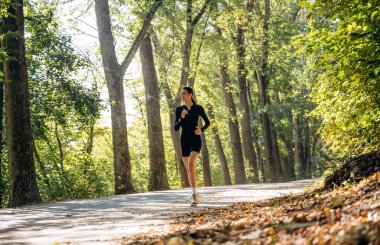 Aktif koşu, koşu. Genç, sıska kadın dışarıda siyah spor kıyafetleri giyiyor..