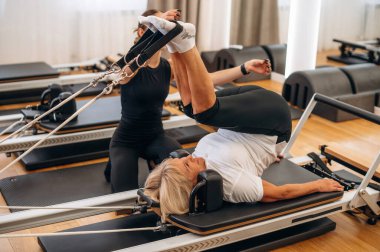 Uzanmak ve bacak egzersizi yapmak. Kadın eğitmen yaşlı kadına yardım ediyor..