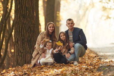 Gündüz vakti, otururken. Mutlu anne, baba ve iki kız çocuk ailesi sonbahar parkında, ormanda, yolda.