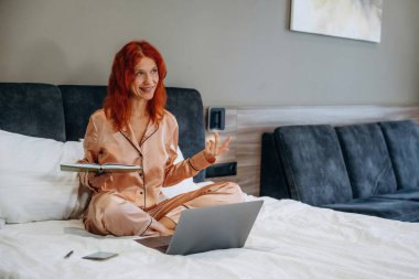 Yatağın üzerinde gümüş renkli bir dizüstü bilgisayar var. Kadın otel odasında, modern iç mekan..
