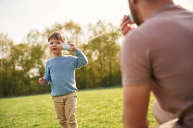 Kağıt bardak telefon kullanarak. Mutlu baba ve oğul yazın sahada eğleniyorlar..