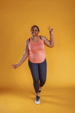 Spor kıyafetleri içinde. Afrikalı Amerikalı kadın sarı arka planda stüdyoda..