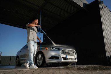 Gümüş renkli yüzey, otomobili yıkıyor. Adam dışarıda arabasıyla bekliyor..