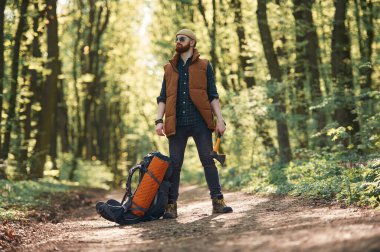 Sarı balta elinde, sırt çantası yerde. Sakallı adam gündüz vakti ormandadır..