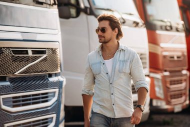 Güneş gözlüklü, havalı görünüyorsun. Kamyon şoförü açık havada nakliye aracının yanında..