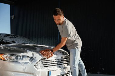 Otomobili yıkamaya odaklanmış. Adam dışarıda arabasıyla bekliyor..