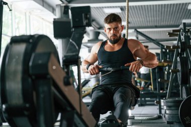 Oturmak, dayanıklılık egzersizi yapmak. Güçlü kaslı adam spor salonunda çalışıyor..