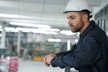 Korkuluklara yaslanarak. Fabrika işçisi kasketli bir şekilde içeride..