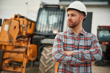 Beyaz kasketli. Adam traktörle birlikte. Tarım işçisi.