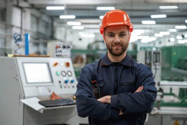 Kollarını kavuşturmuş duruyorsun. Fabrika işçisi kasketli bir şekilde içeride..