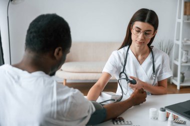 Masanın başında oturuyor. Kadın doktor bir erkeğin kan basıncını ölçer..