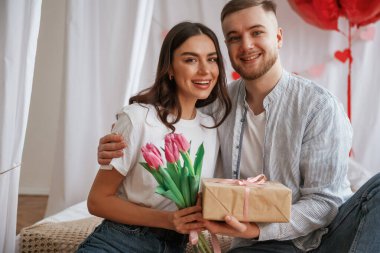 Hediye kutusu ellerinde, bayramı kutluyorlar. Genç çift evde birlikteler..