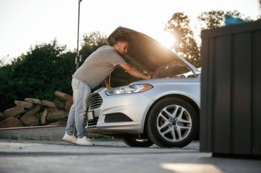 Güzel güneş ışığı. Kaput açıldı, adam otomobili tamir ediyor. Adam dışarıda arabasıyla bekliyor..