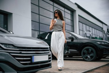 Beyaz bir kadeh ile. Çekici genç bayan dışarıda, yepyeni arabasının yanında..