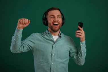 Gülümsüyor, müzikten zevk alıyor. Adam stüdyoda arka planda duruyor..