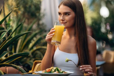 Restoranın dışında. Güzel genç bayan masanın yanında oturuyor..