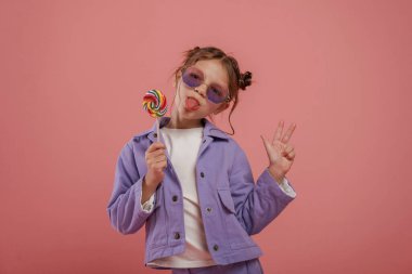 Şekerlerin tadını çıkarıyorum. Şirin küçük kız pembe arka plana karşı..