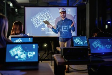 Bir şeyleri açıklamak. Erkek mimar, insanlar için mavi projektör üzerinde inşaat alanı projesi gösteriyor.