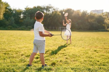 Raketler ellerinde, badminton oynuyorlar. Mutlu çocuklar yaz tarlasında.